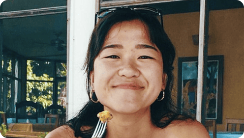 Person smiling while holding a fork with food in an indoor setting.