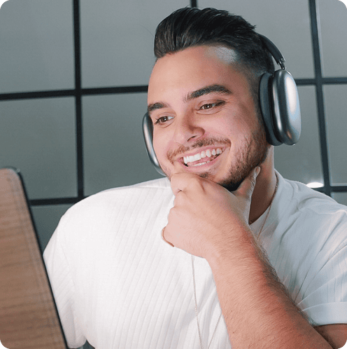 Person wearing headphones, smiling, and looking at a laptop screen.