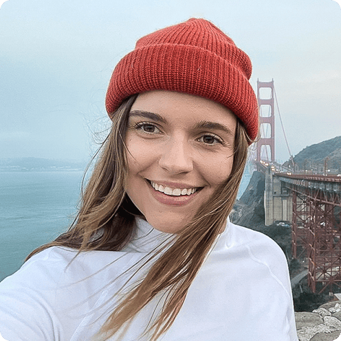 Person wearing a red beanie smiles at the camera with the Golden Gate Bridge and a cloudy sky in the background.