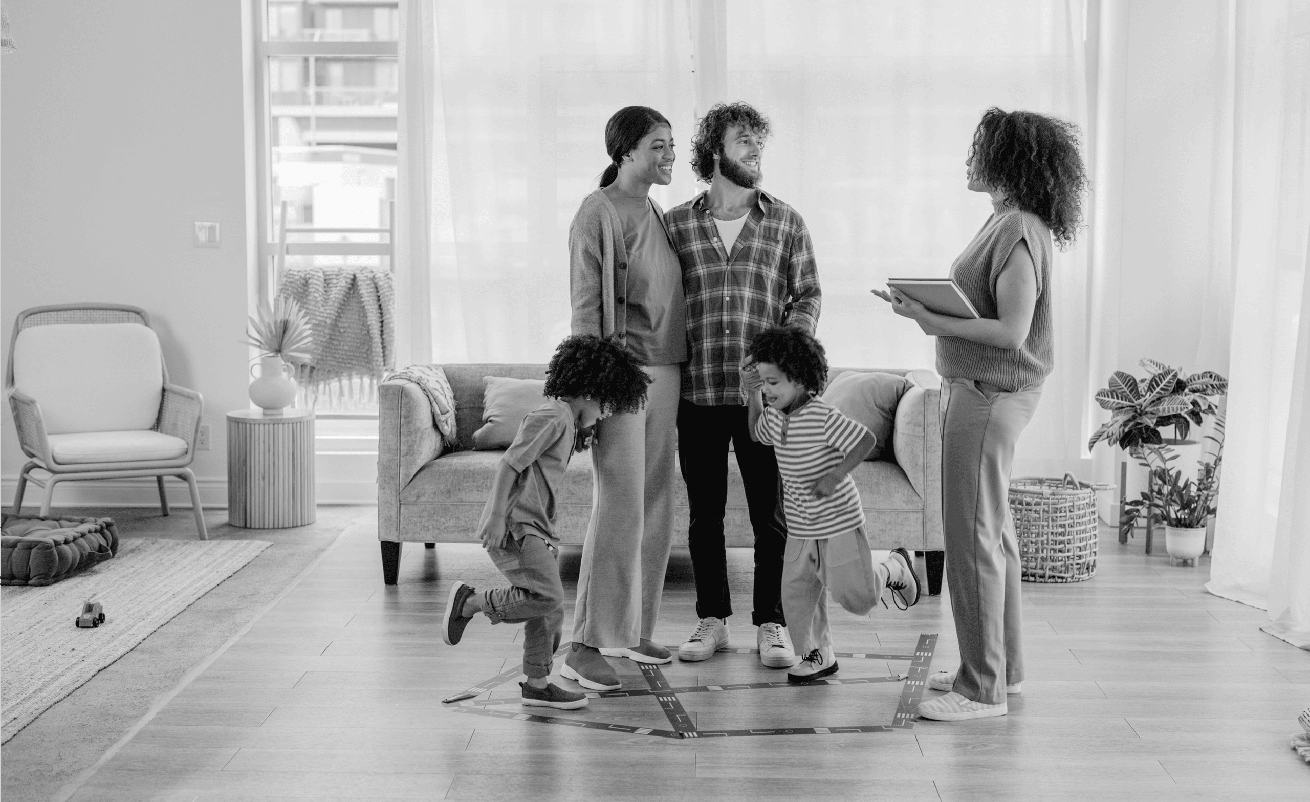 A family with two children interacts with a woman holding a clipboard in a living room. The children play inside a taped area on the floor.